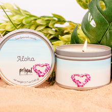 Load image into Gallery viewer, Hand-poured candle labeled &#39;Aloha&#39; with a lit wick, surrounded by pink flowers and green leaves.