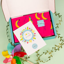 Load image into Gallery viewer, Open box with colorful greeting card and decorative items on a light green background