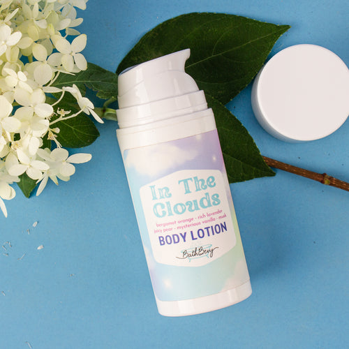 Body lotion bottle labeled 'In The Clouds' on a blue background with flowers and leaves.