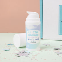 Load image into Gallery viewer, A pump bottle of body lotion labeled &#39;In The Clouds&#39; positioned on a surface with decorative stars, against a pink and blue background.