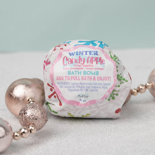 A packaged bath bomb with 'Winter Candy Apple' label, surrounded by decorative pearls on a light background.