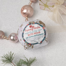 Load image into Gallery viewer, A packaged bath bomb with pomegranate and spice botanical print design, labeled &#39;Pomegranate Bath Bomb&#39;, placed on a decorative setting with pearls and greenery.