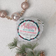 Load image into Gallery viewer, A packaged bath bomb with &#39;MULBERRY BATH BOMB&#39; label, placed on a surface with pine branches and decorative balls, indicating it is meant to add to a full bath and enjoy the fruit-themed scent and therapeutic benefits.