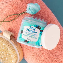 Load image into Gallery viewer, Blue Morpho whipped soap scrub with a brush and towel on a pink surface