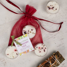 Load image into Gallery viewer, White candles with red berries in a red drawstring bag on a light wooden surface.