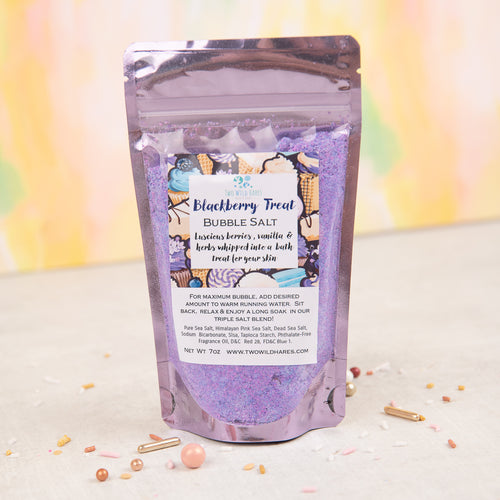 A package of BLACKBERRY TREAT BUBBLE SALT by Two Wild Hares, featuring a colorful design with bath bubbles and blackberries, placed on a surface with confetti scattered around.